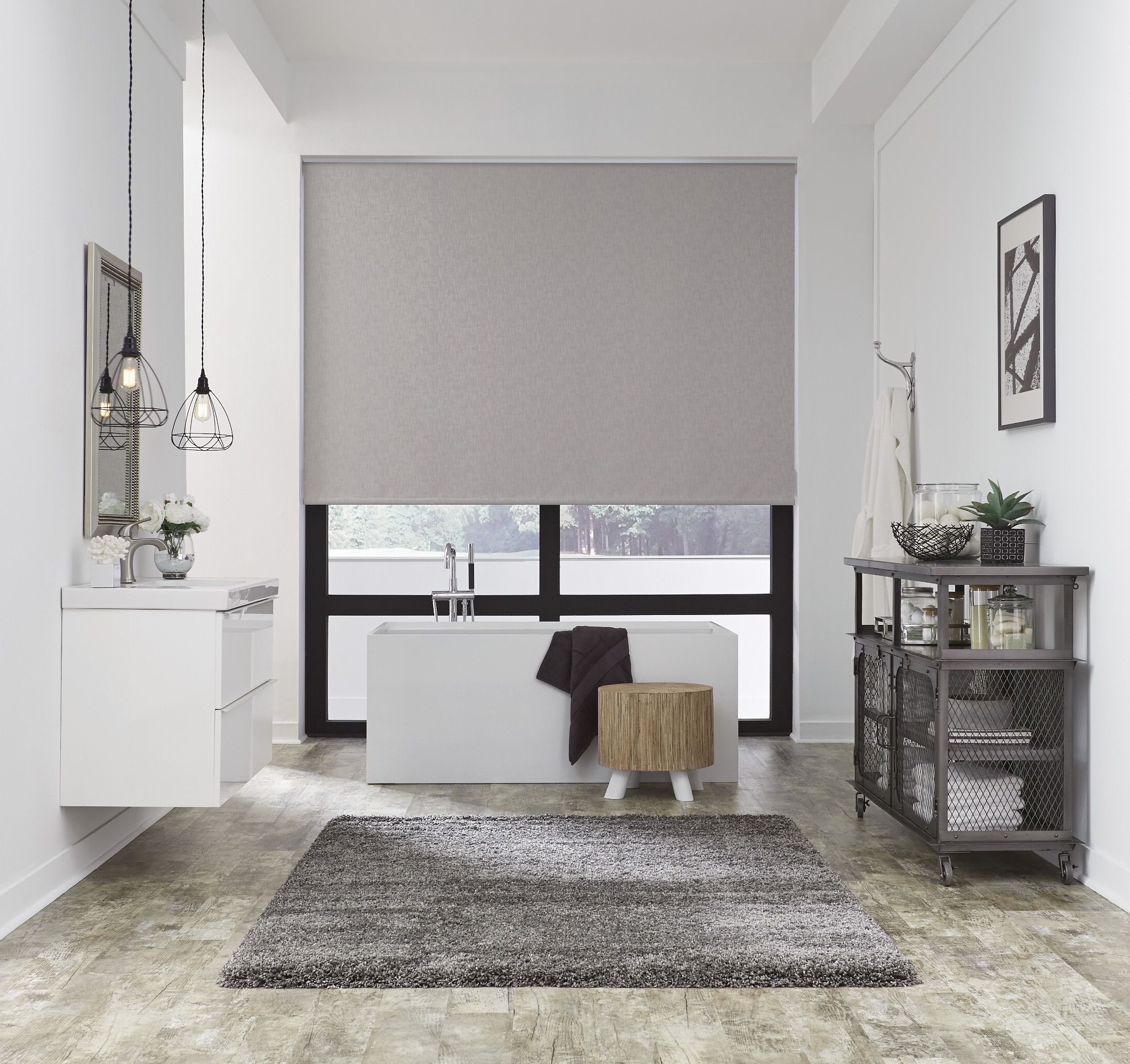 Elegant bathroom with a large grey motorized roller shade fully drawn above a freestanding soaking tub, pendant lights, and clean white walls